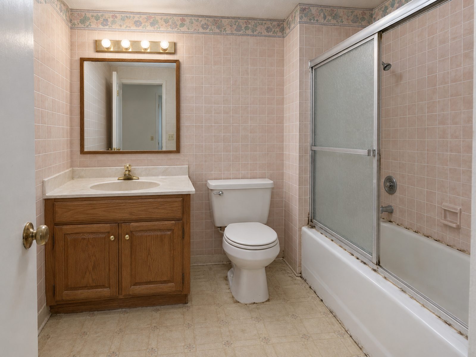 Dated bathroom with pink wall tile and an oak vanity before remodeling